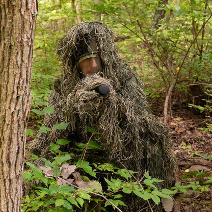 Man in a ghillie suit blending into the outdoor environment.